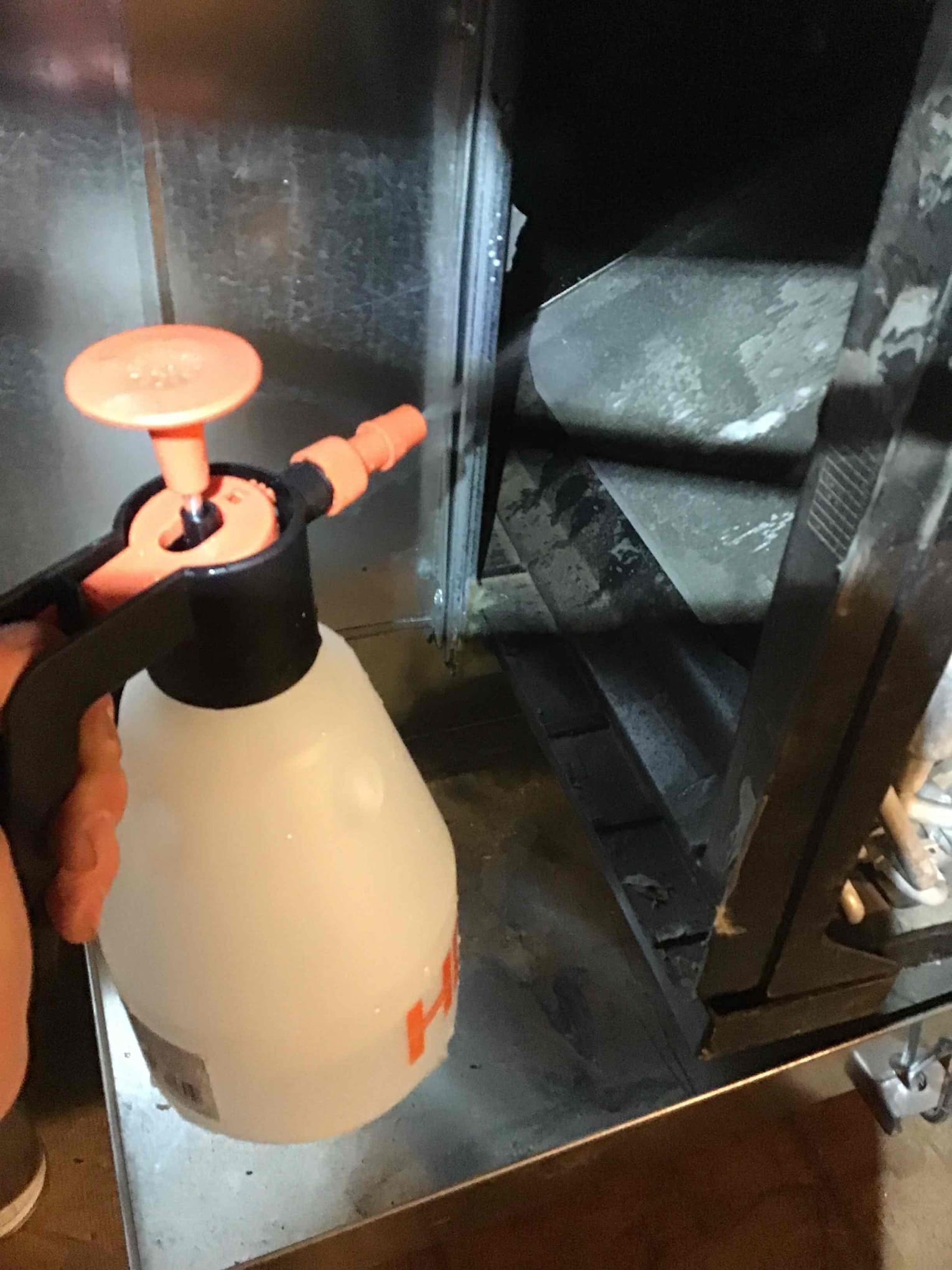 Handheld pump sprayer applies cleaning solution toward the blower wheel inside the air handler cabinet.
