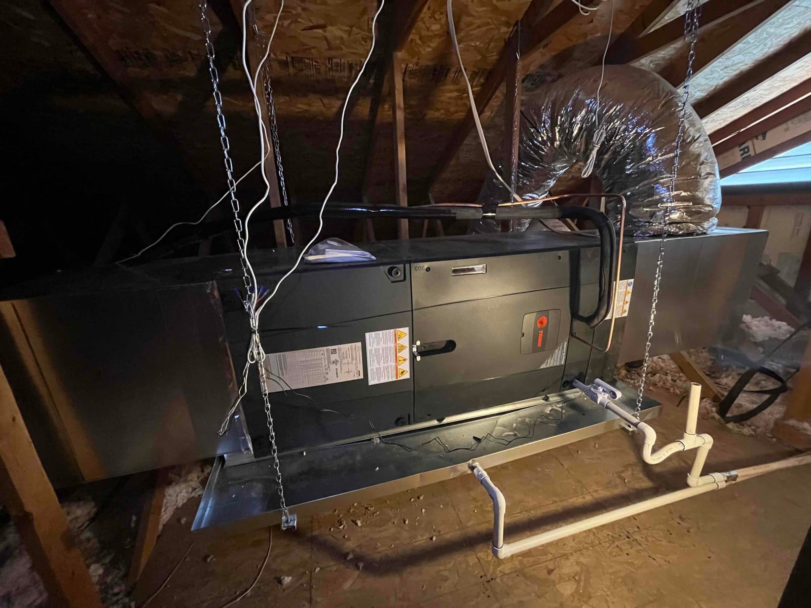 New air handler suspended in attic with insulated duct connection, sealed supply and return plenums, and newly installed condensate drain assembly.