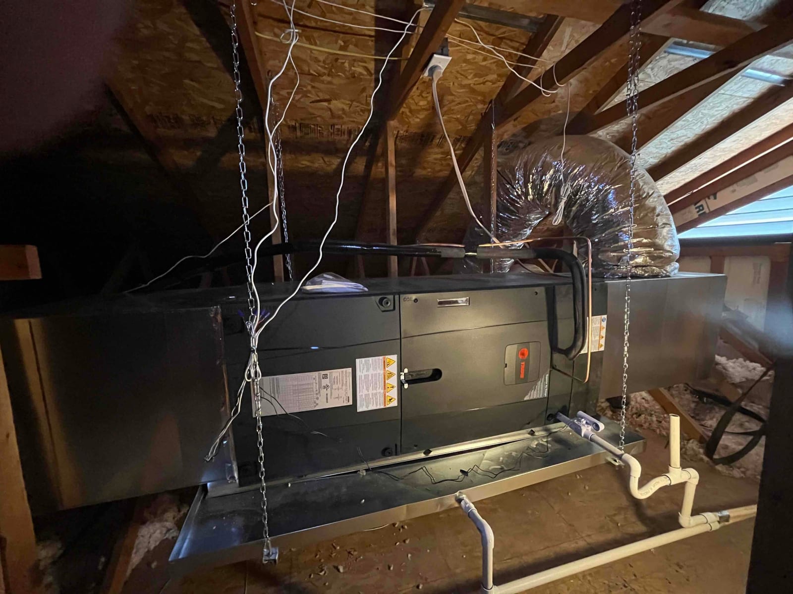 New air handler suspended in the attic with insulated return duct, drain pan, and condensate piping connected and supported.