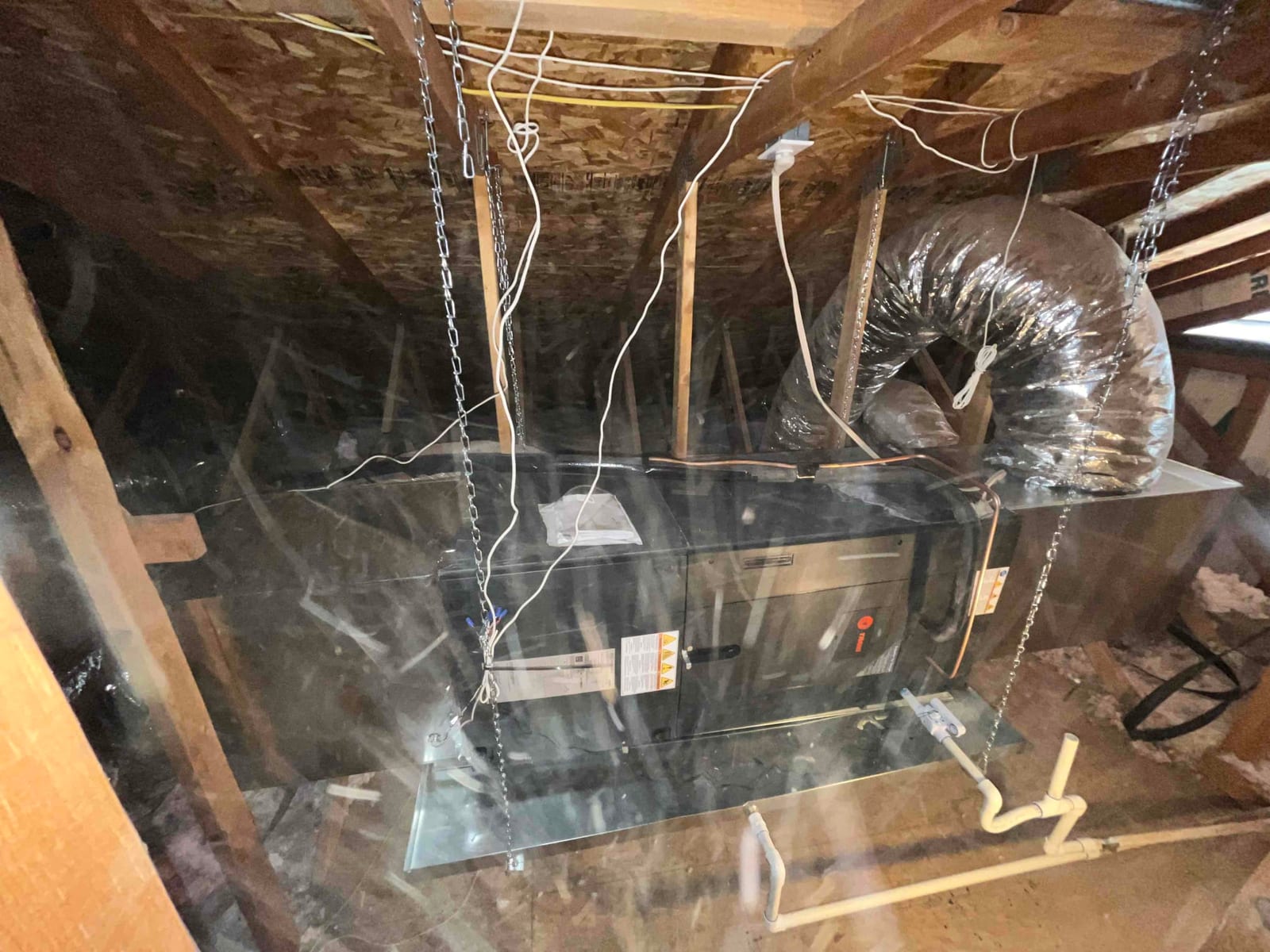New air handler suspended on hanging kit in attic with flexible duct connection and condensate drain piping installed.