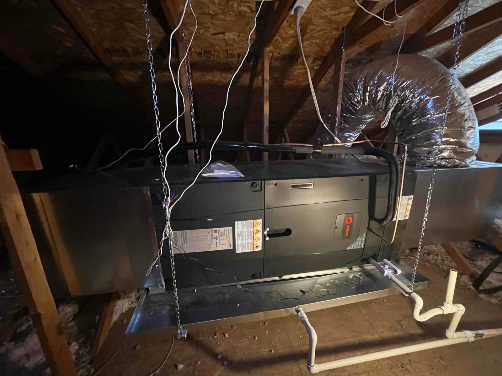 New attic air handler hung with chains, insulated duct connection, and installed condensate drain with cleanout and trap.