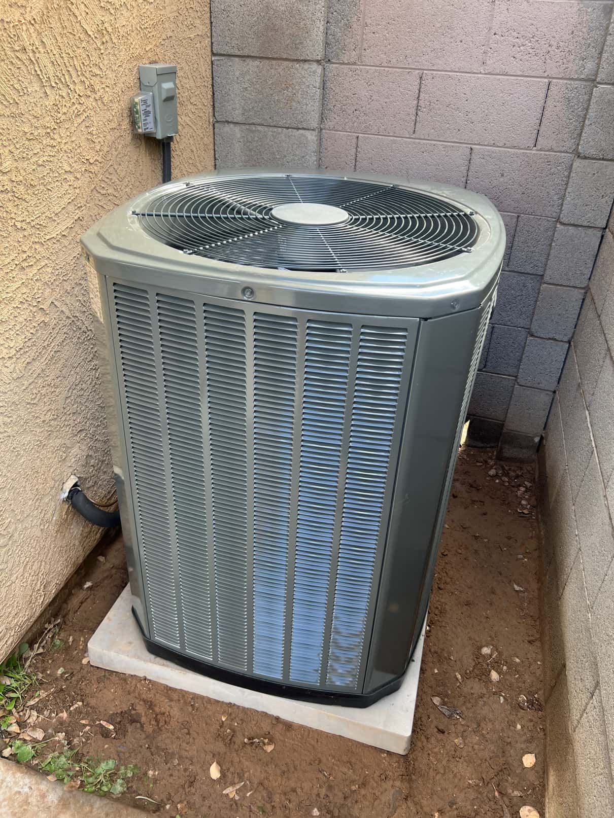 New outdoor heat pump condenser set on a level pad with electrical disconnect mounted and insulated line set routed through the wall.