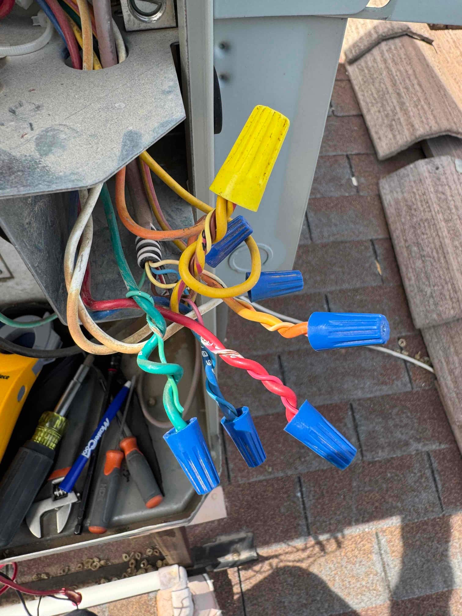 Open electrical compartment on rooftop condenser shows multiple wire connections secured with twist-on wire connectors in various colors.