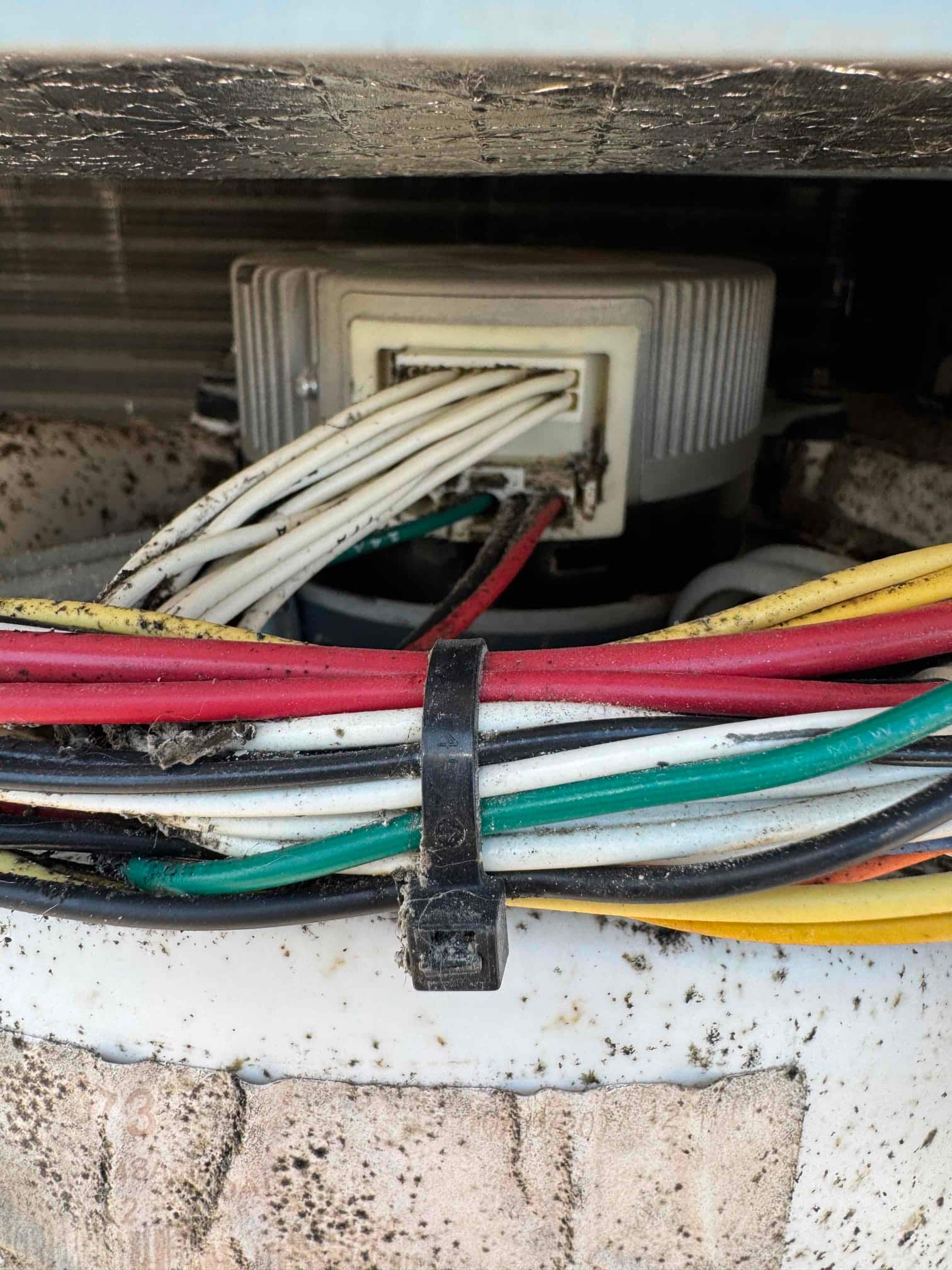 Outdoor condenser fan motor wiring harness with multiple colored leads and connector, showing dirt accumulation on the housing and wires.