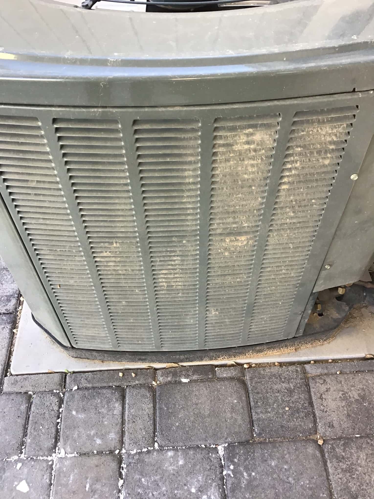 Outdoor condenser unit with louvered panels showing dust and dirt on the intake grille.