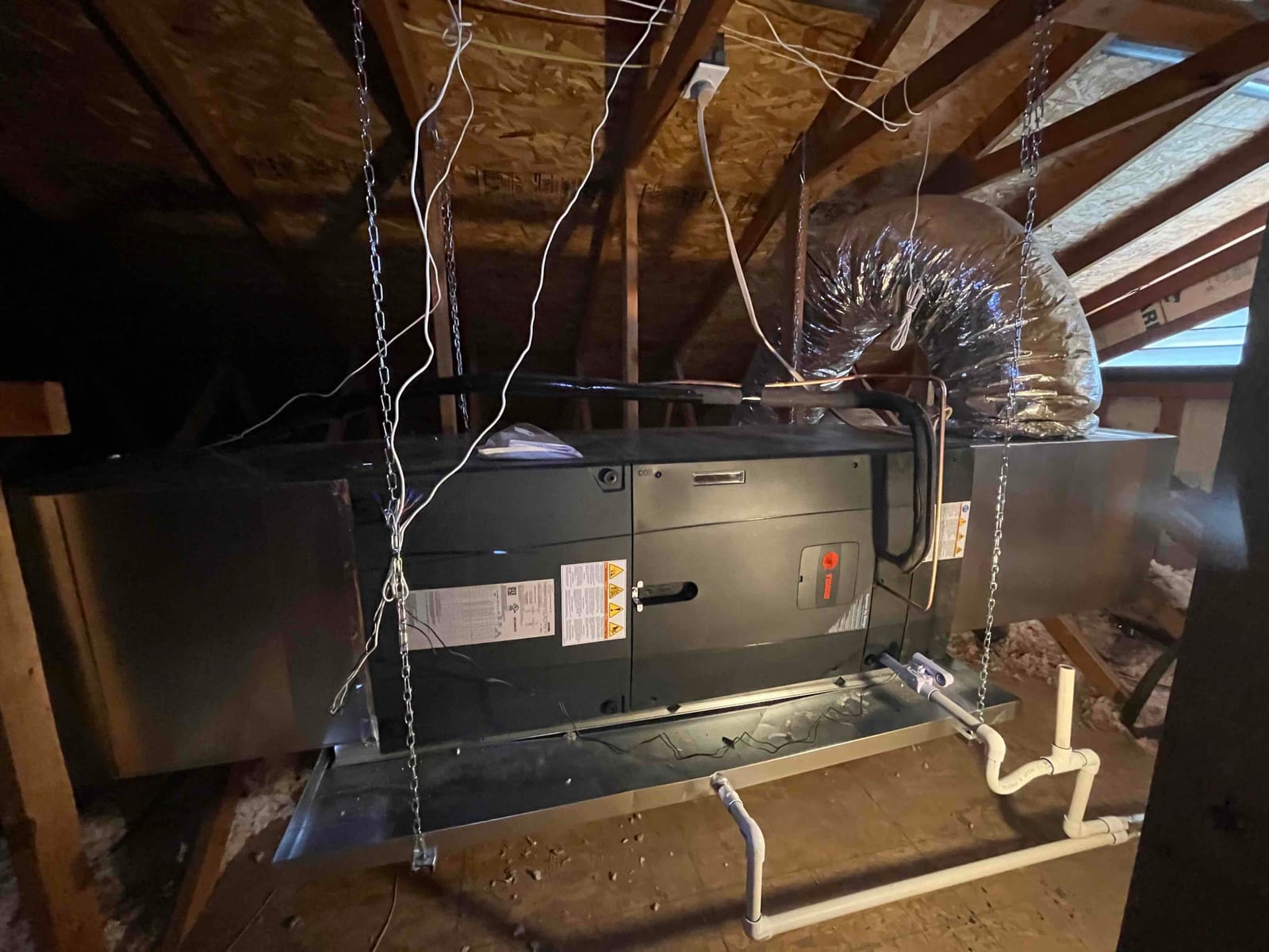 Suspended air handler installed on hangers with insulated duct connection and newly plumbed condensate drain over a secondary drain pan.