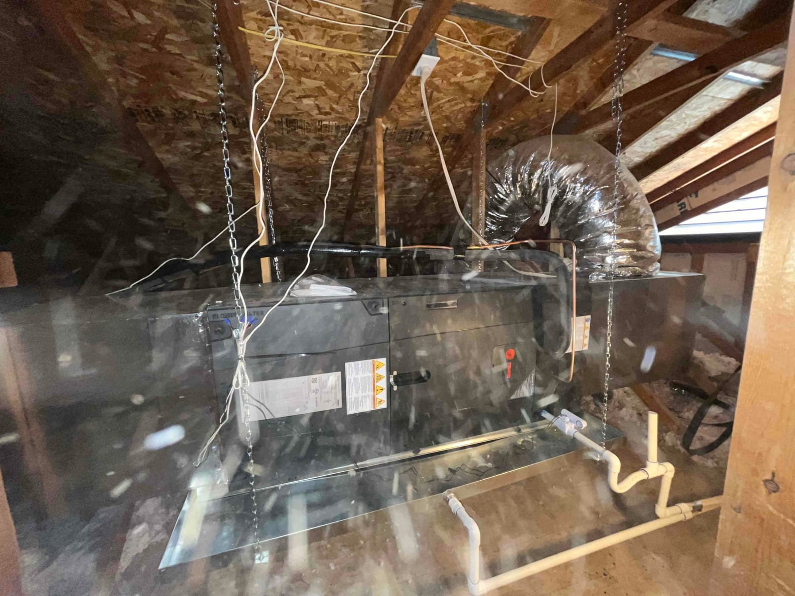 Suspended attic air handler installed with insulated flex duct, secondary drain pan, and PVC condensate drain piping.