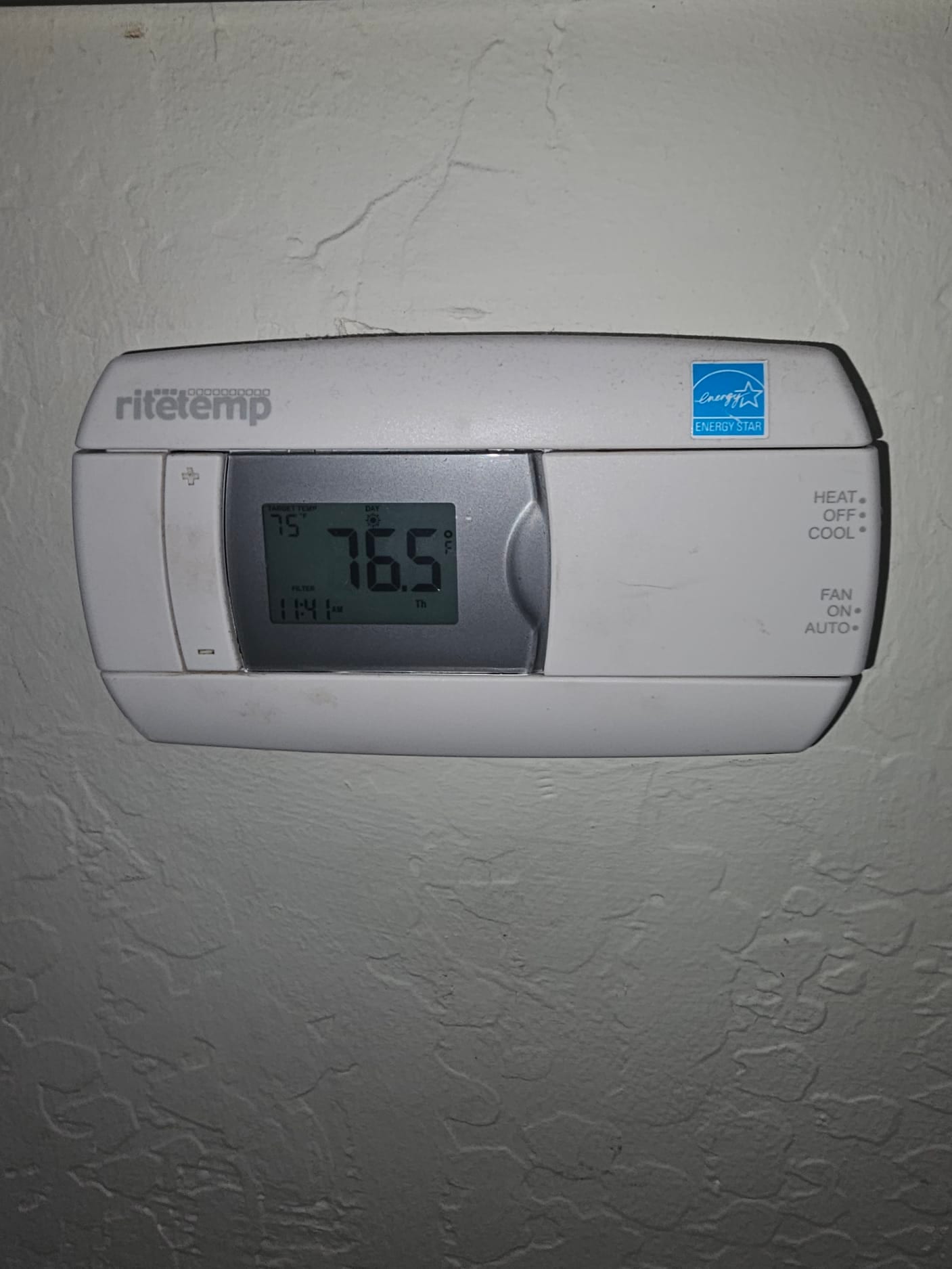 Wall-mounted digital thermostat shows 76.5°F room temperature with HEAT-OFF-COOL selector and fan on AUTO.