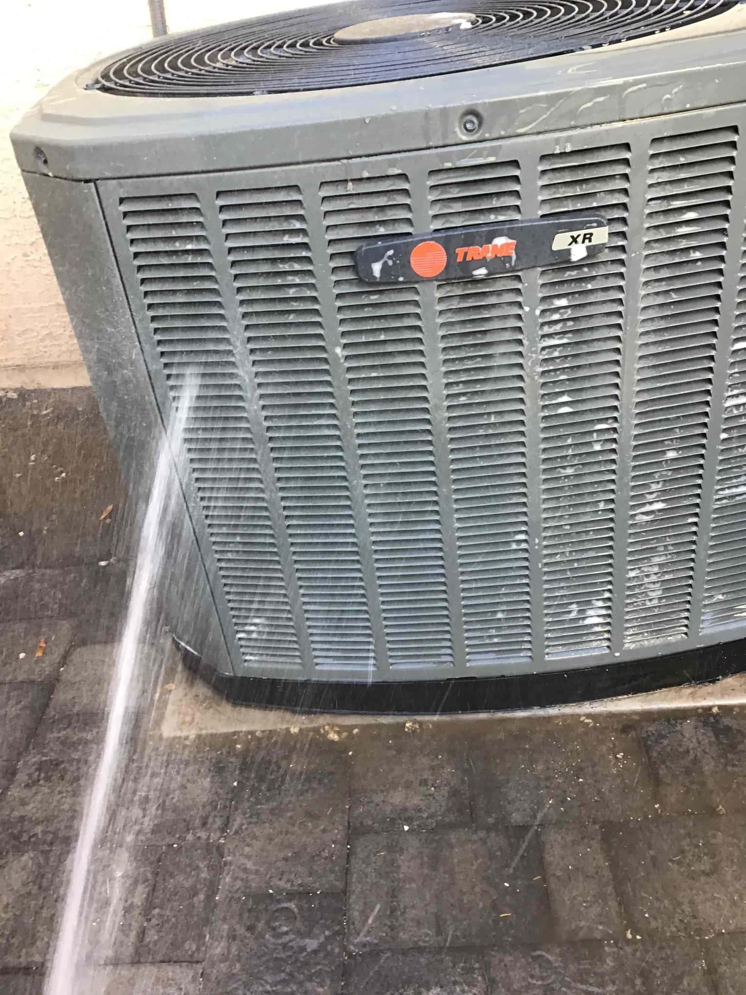 Water spray hitting the outdoor condenser coil grille on a residential air conditioning unit.