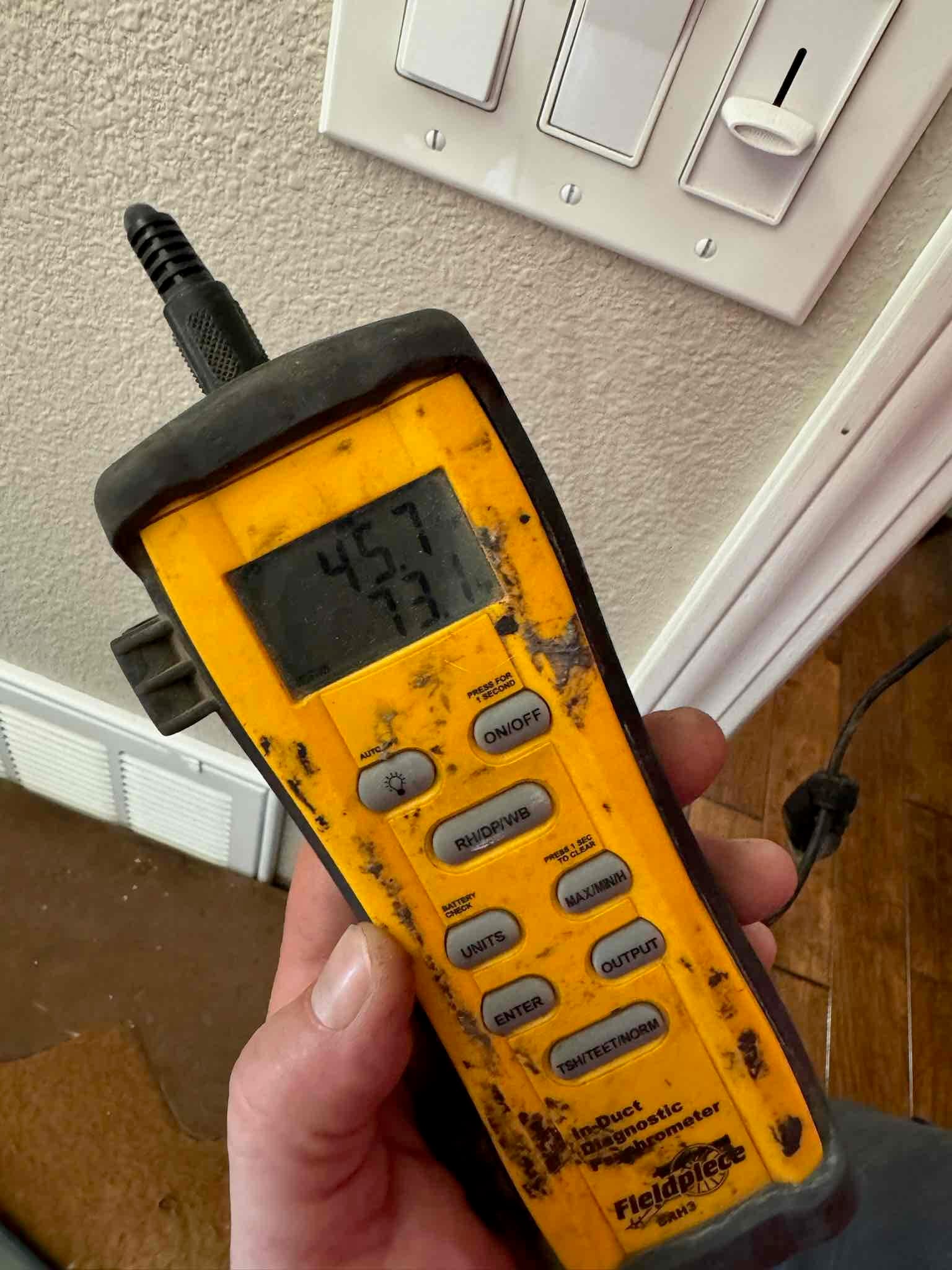 Handheld digital thermometer shows air temperature reading near a return grille during HVAC commissioning.