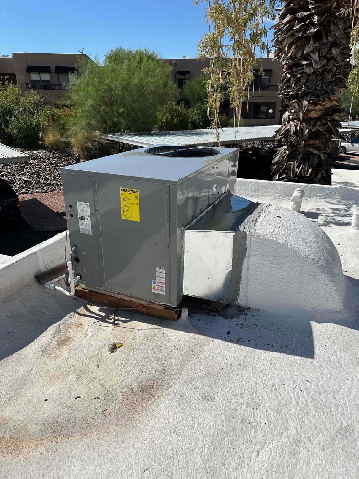 New packaged rooftop heat pump set on curb with connected duct transition and condensate drain routed along the roof.