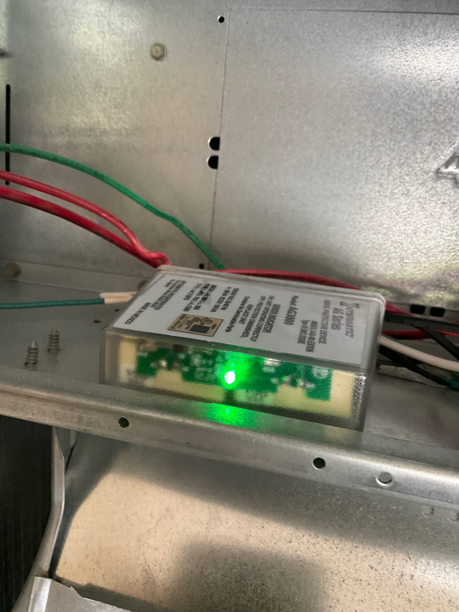Small electronic module with green indicator light mounted inside the air handler compartment, with red and green wires routed nearby.