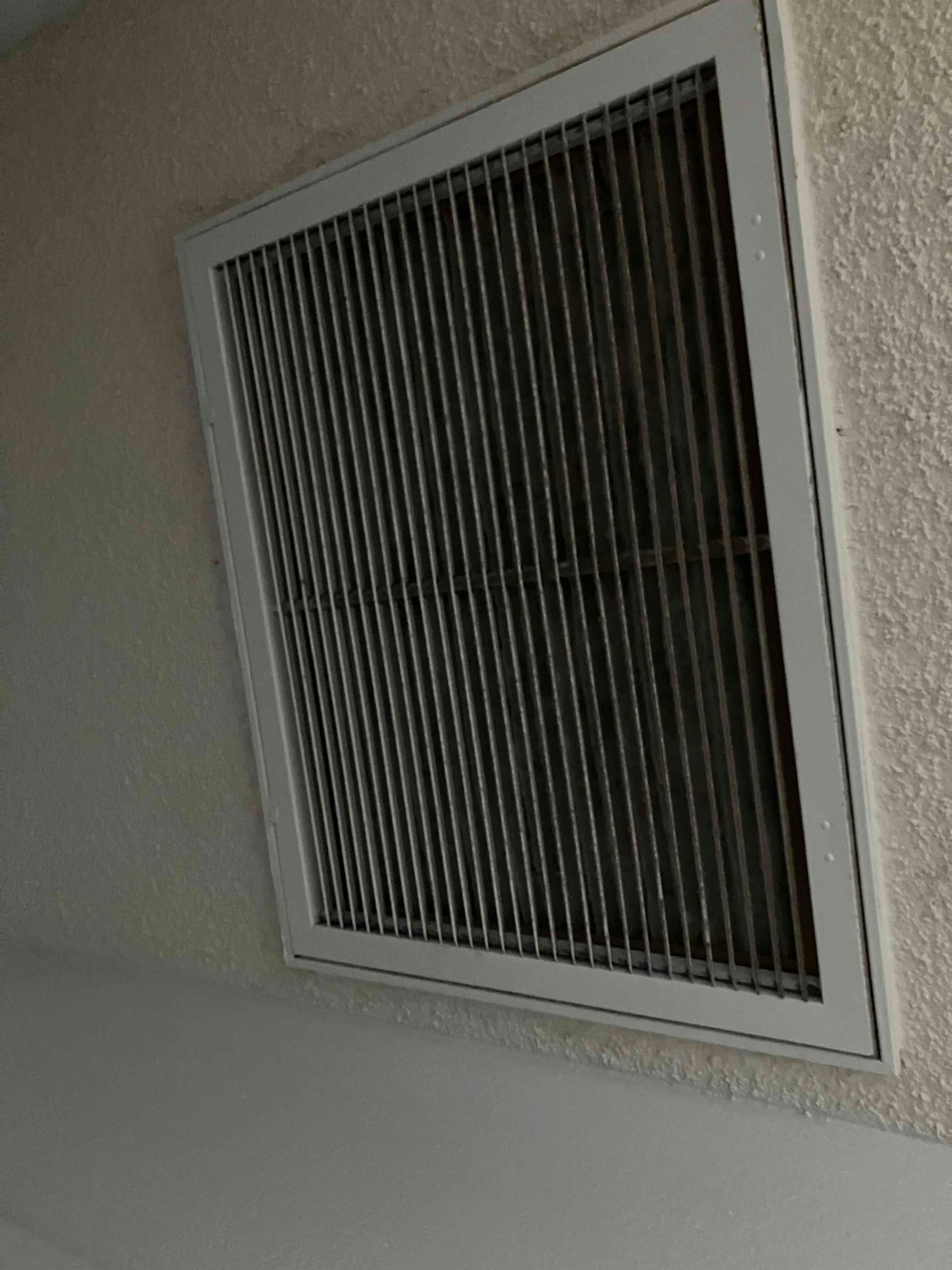 Ceiling-mounted return air grille installed flush with textured drywall, showing straight louvers and finished trim frame.