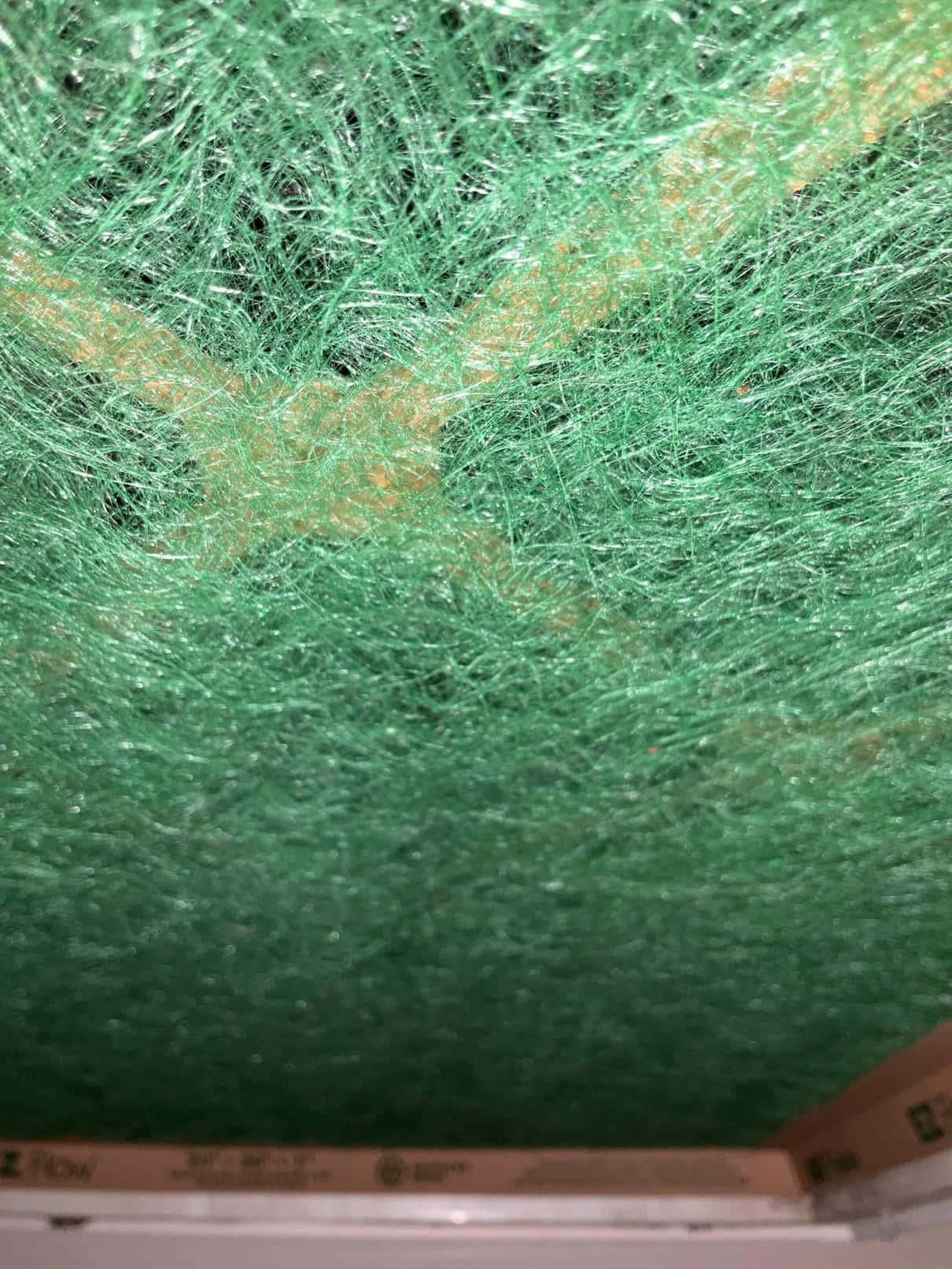 Close-up of green fiberglass HVAC air filter media within a cardboard frame at the grille.
