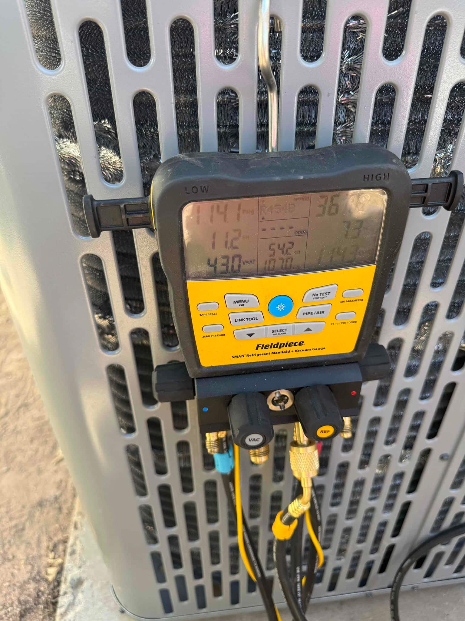 Digital manifold connected to the outdoor unit shows operating pressures with low and high sides during system commissioning.