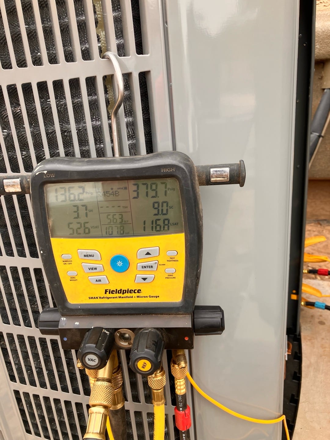 Digital manifold gauges on the condenser show operating pressures during system commissioning, with refrigerant type indicated on the display.