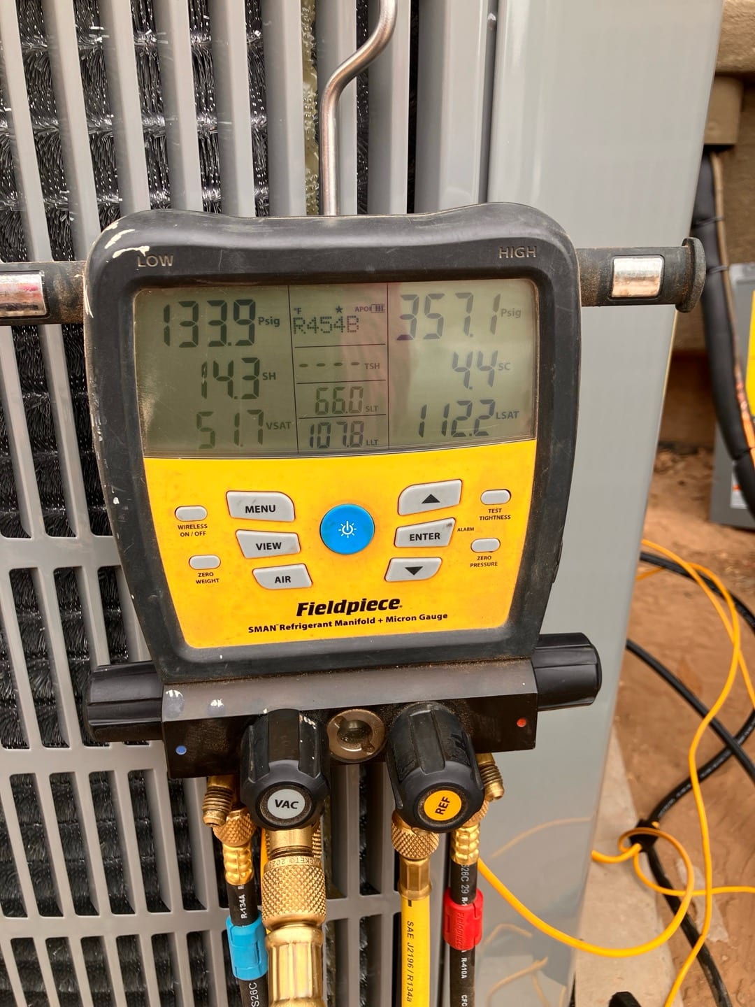 Digital manifold shows operating pressures on an outdoor condenser during commissioning, with R-454B selected and superheat and subcooling displayed.