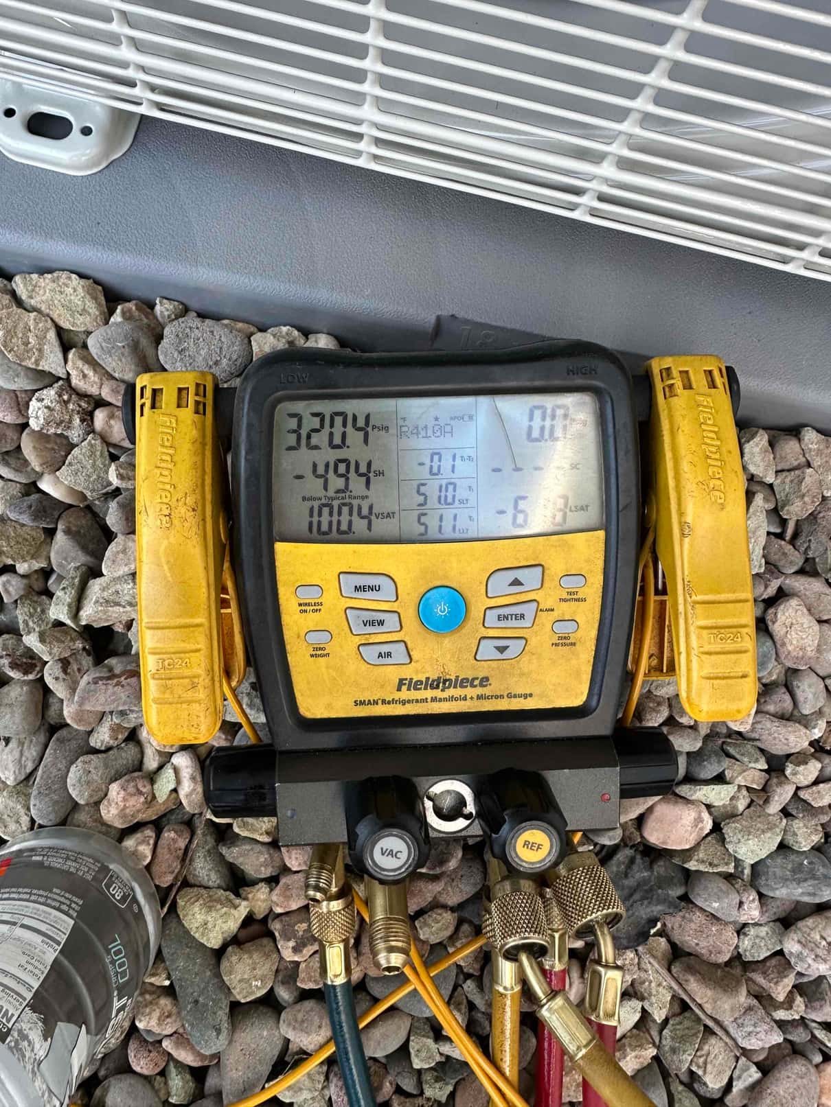 Digital manifold shows system operating pressures with clamps installed on lines during refrigerant commissioning at the outdoor unit.