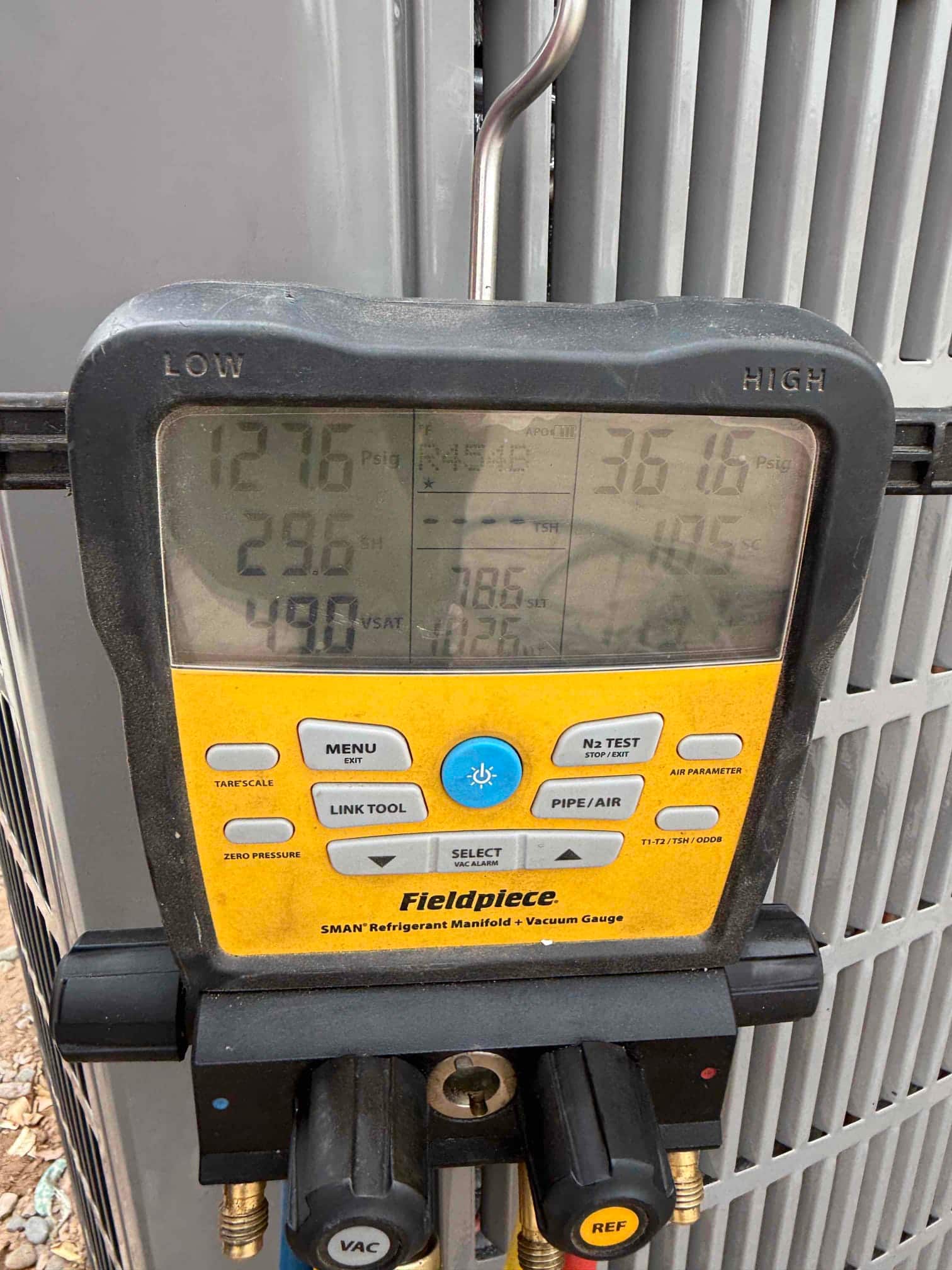 Digital manifold shows system operating pressures while connected at the outdoor unit during commissioning.