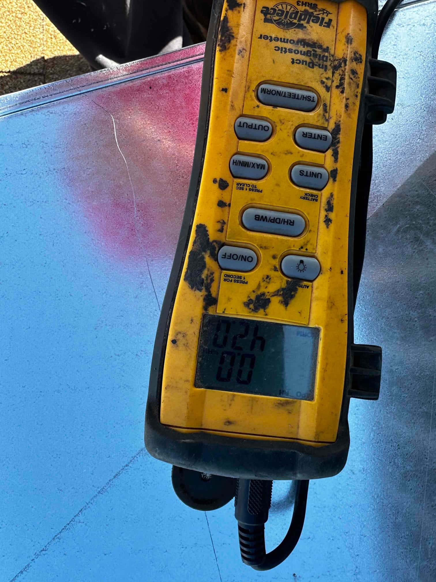 Digital tachometer resting on sheet metal shows 02h and 00 on its display during commissioning checks.