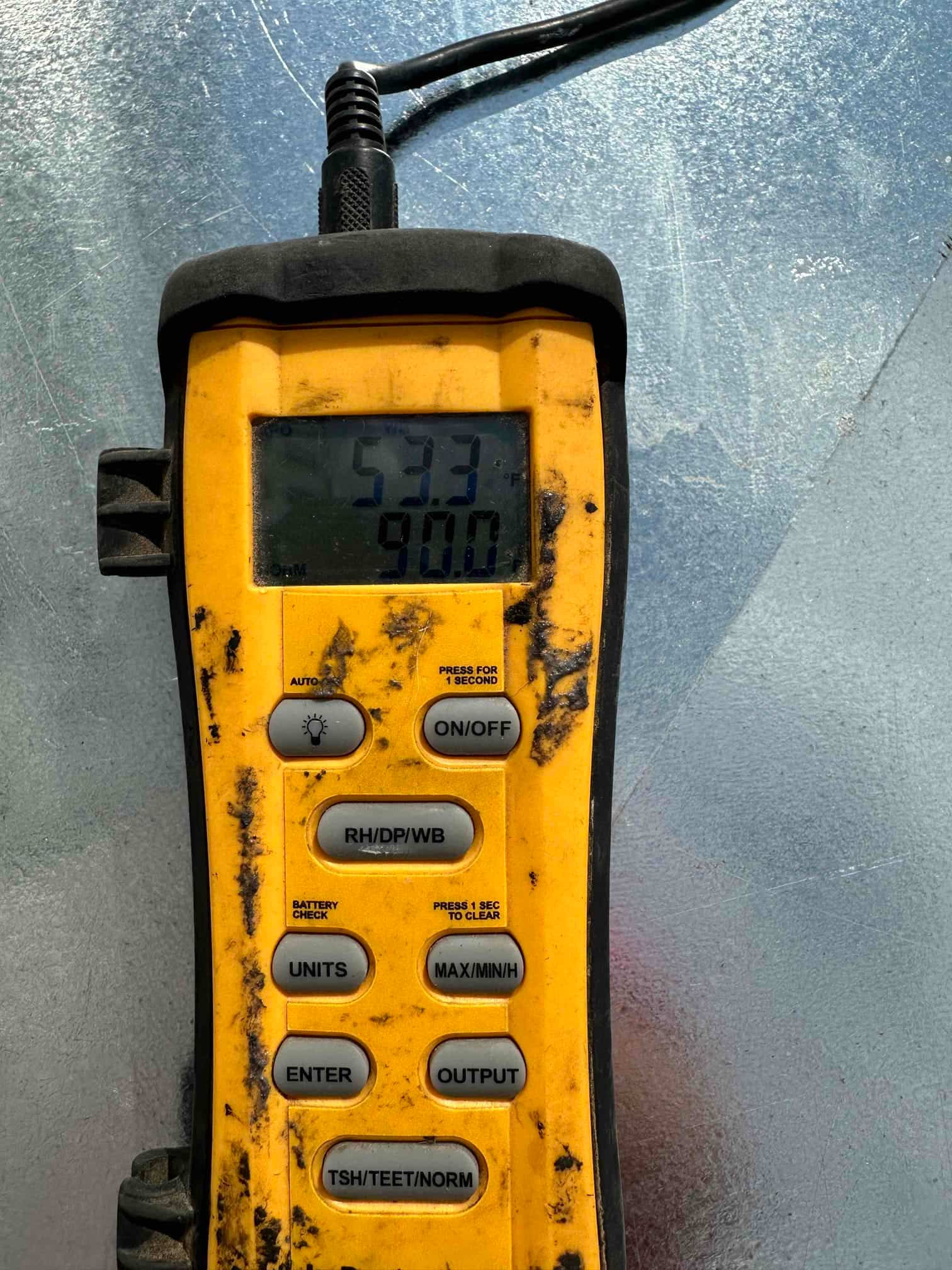 Digital thermometer displays 53.3°F during air temperature check at the HVAC system, documenting cooled supply air performance.