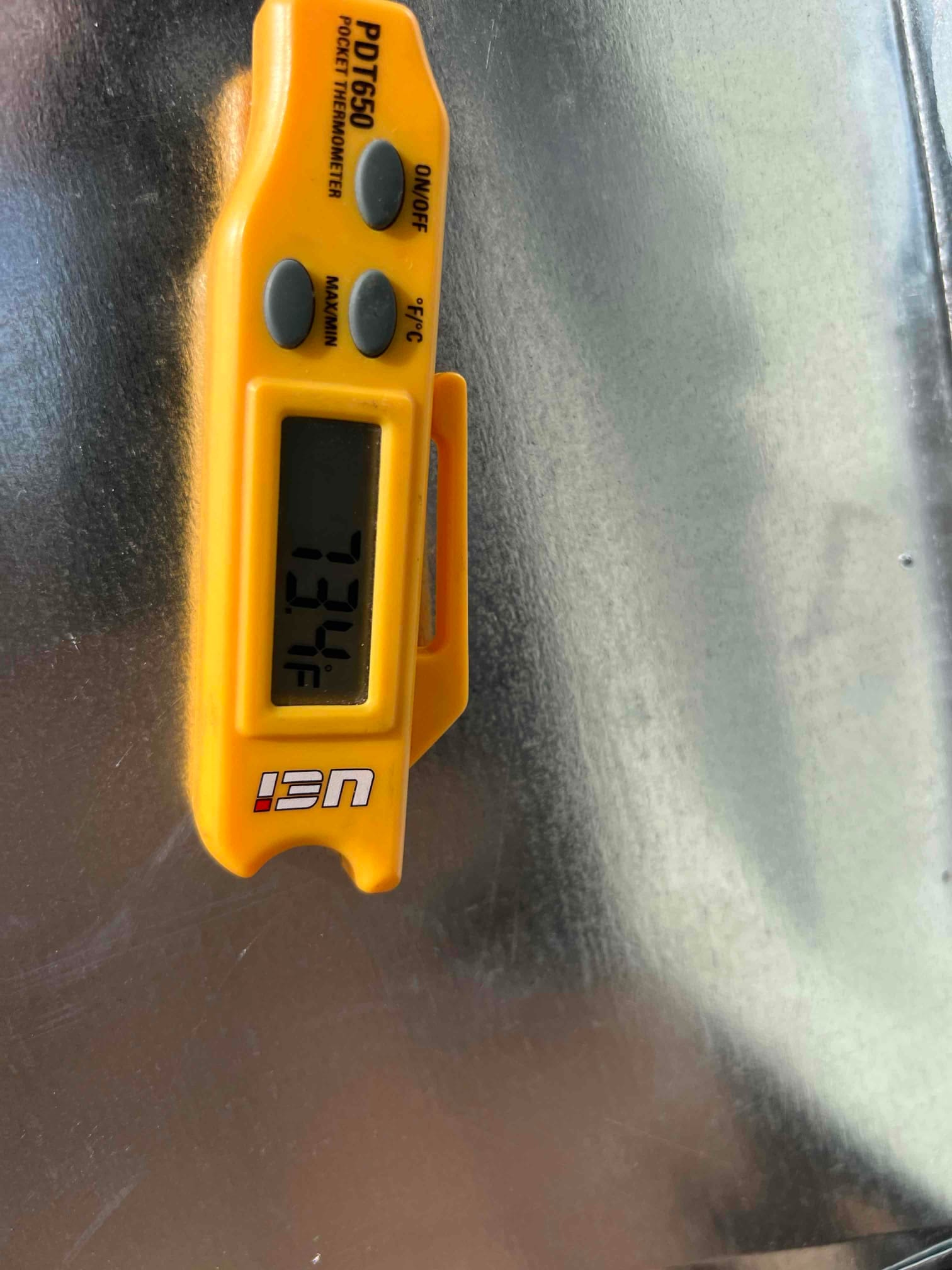 Digital thermometer reads 73°F while measuring air temperature on a metal duct surface during commissioning.