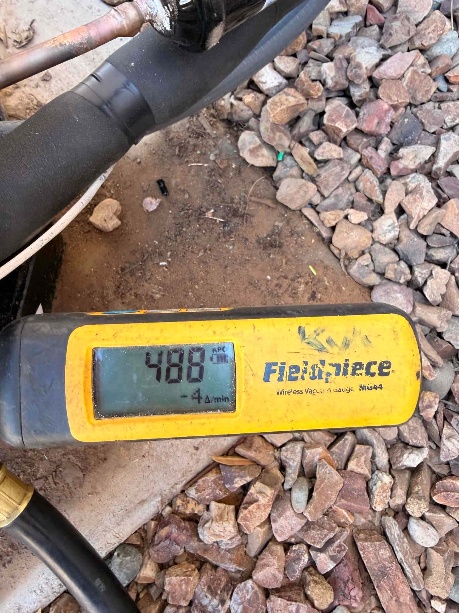 Digital vacuum gauge connected at the condenser shows 488 microns, confirming a deep evacuation before refrigerant charging.