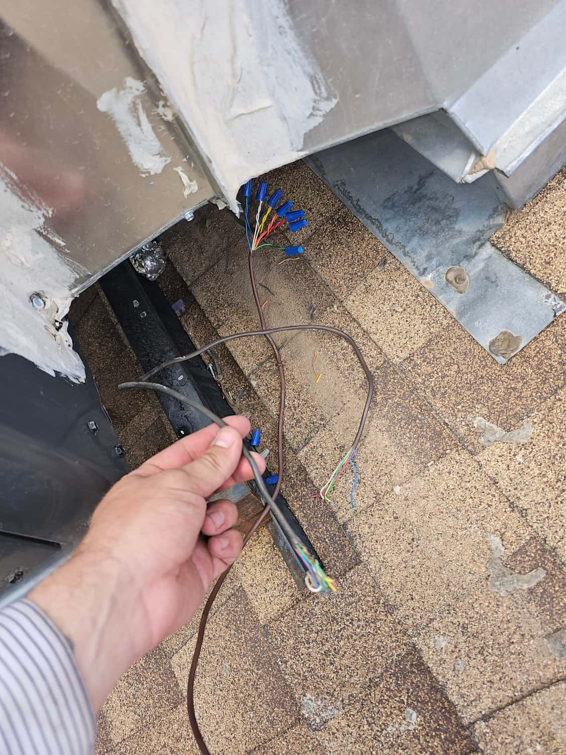 Exposed control wiring and wire nuts at rooftop HVAC penetration, with a technician hand holding a cable.