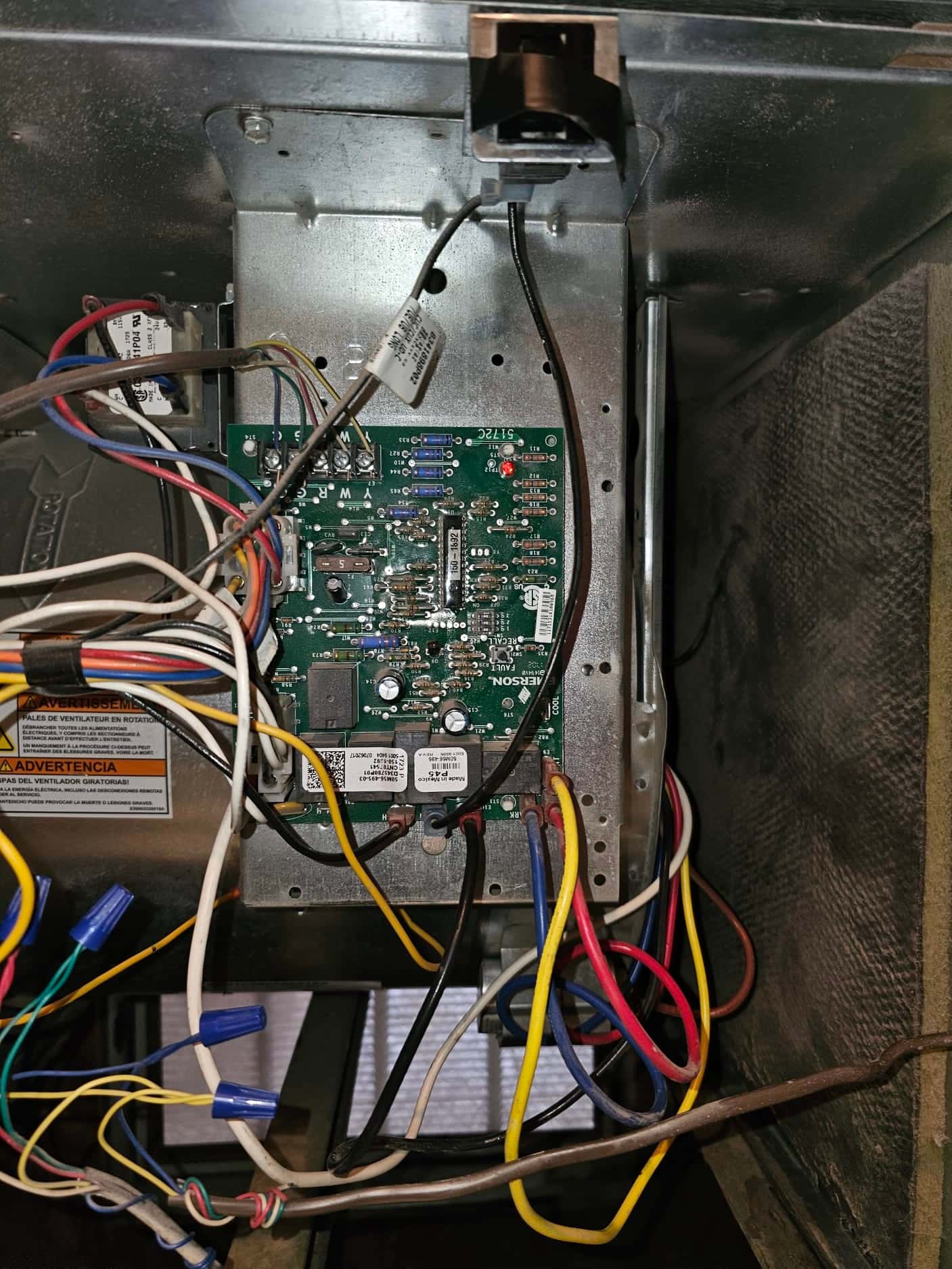 Furnace control board inside the air handler, multiple colored wires connected with wire nuts, red status LED illuminated.