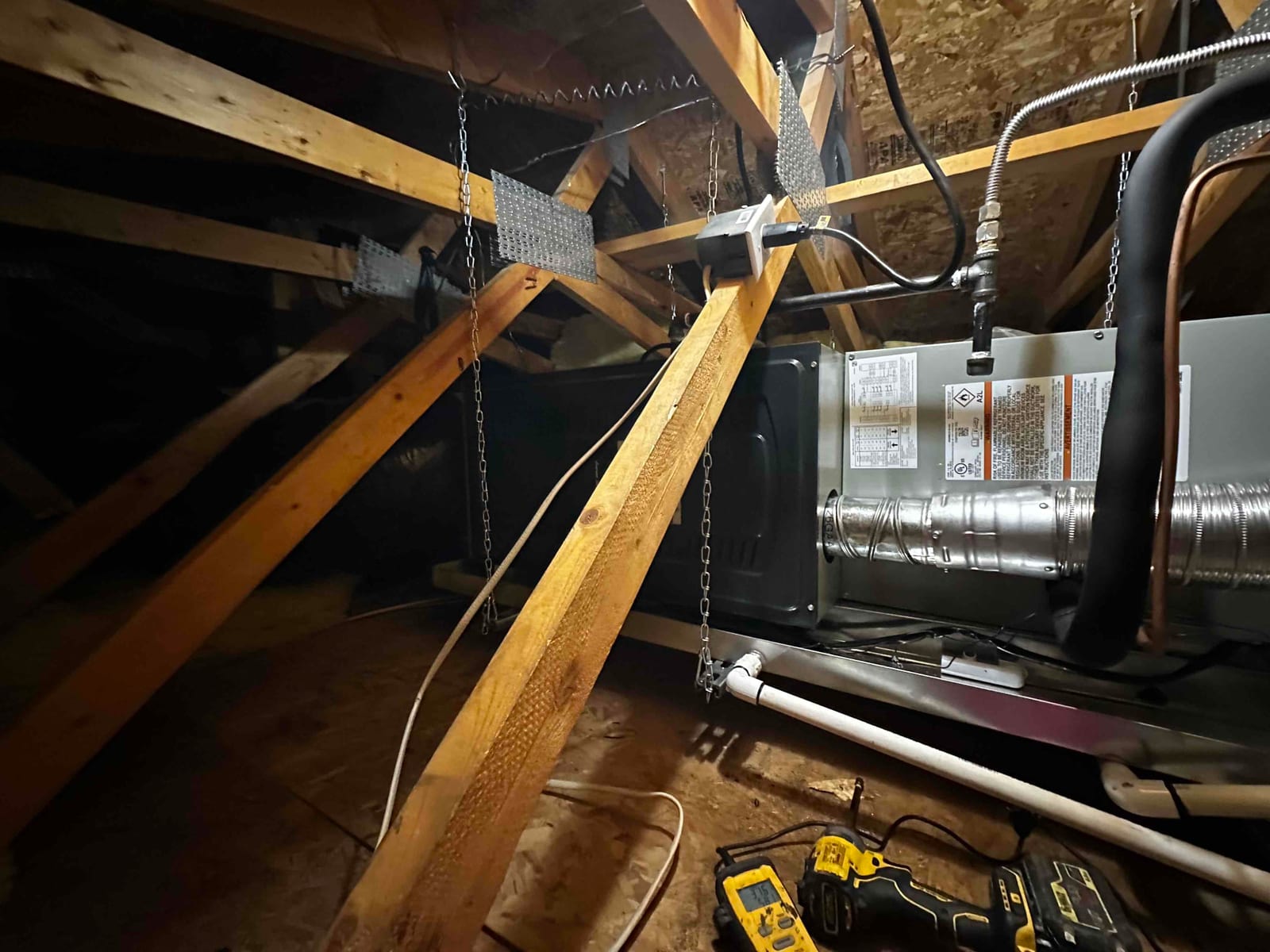 Horizontal air handler suspended in attic with insulated refrigerant lines, metal duct connection, condensate drain, and electrical whip visible.