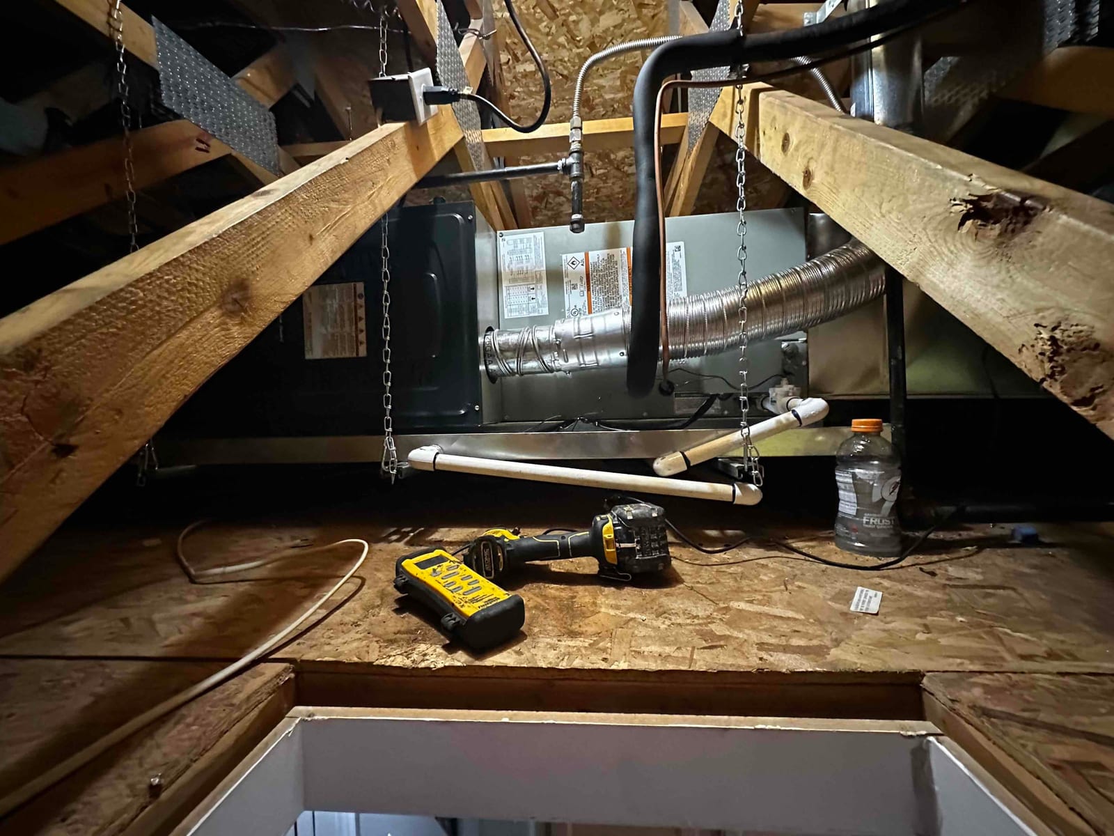 Horizontal air handler suspended in attic with insulated refrigerant lines, flex duct connection, and PVC condensate drain piping installed.