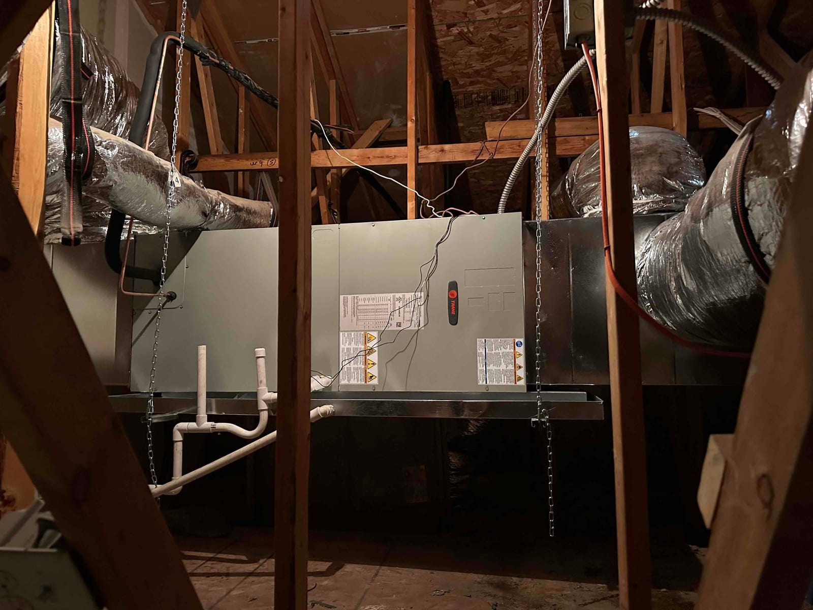 New air handler hung from threaded rods with insulated duct connections and PVC condensate drains installed in the attic.