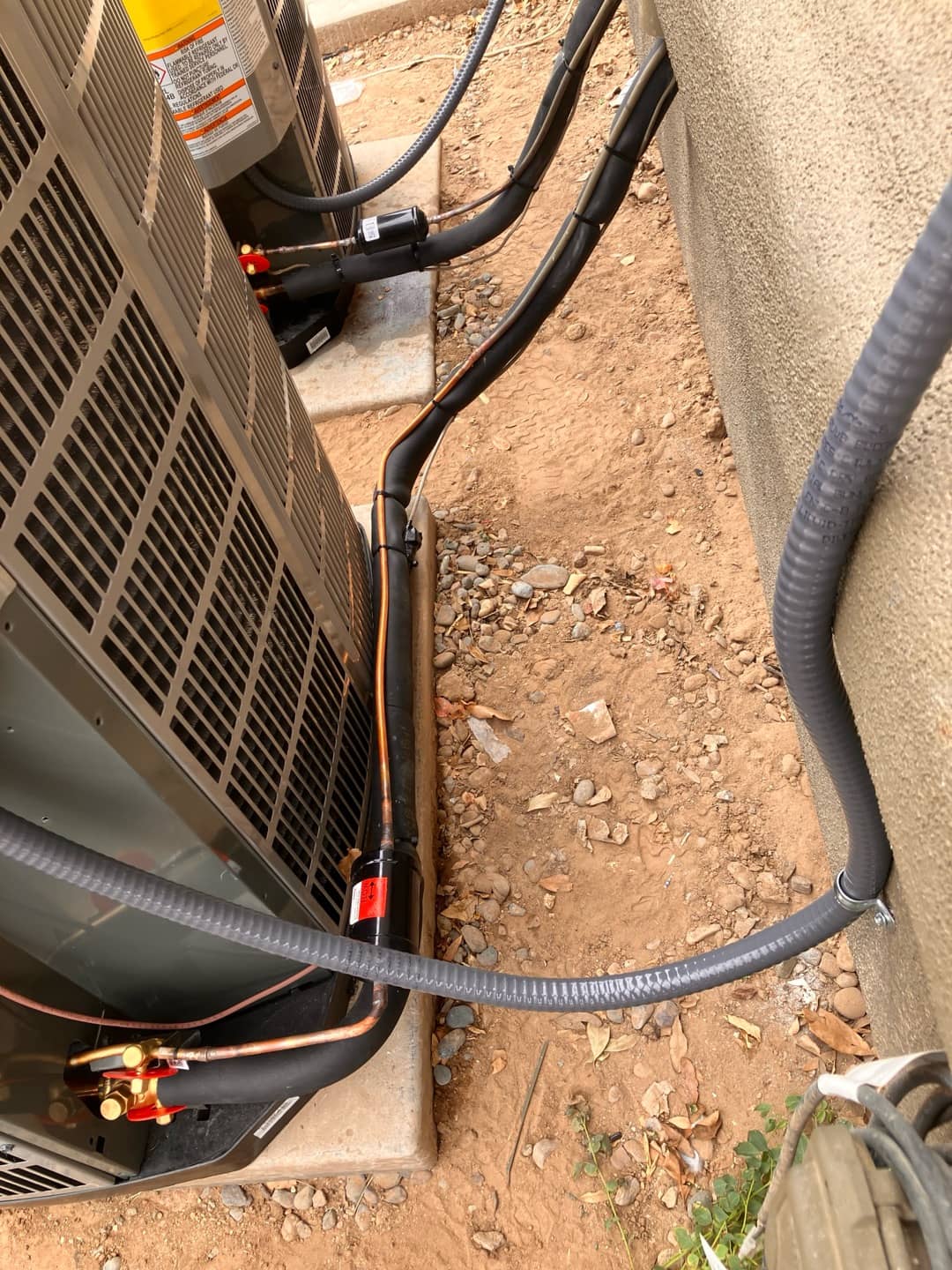 New condensers set on pads with insulated refrigerant lines, filter-driers, and liquid-tight electrical conduits secured to the wall.