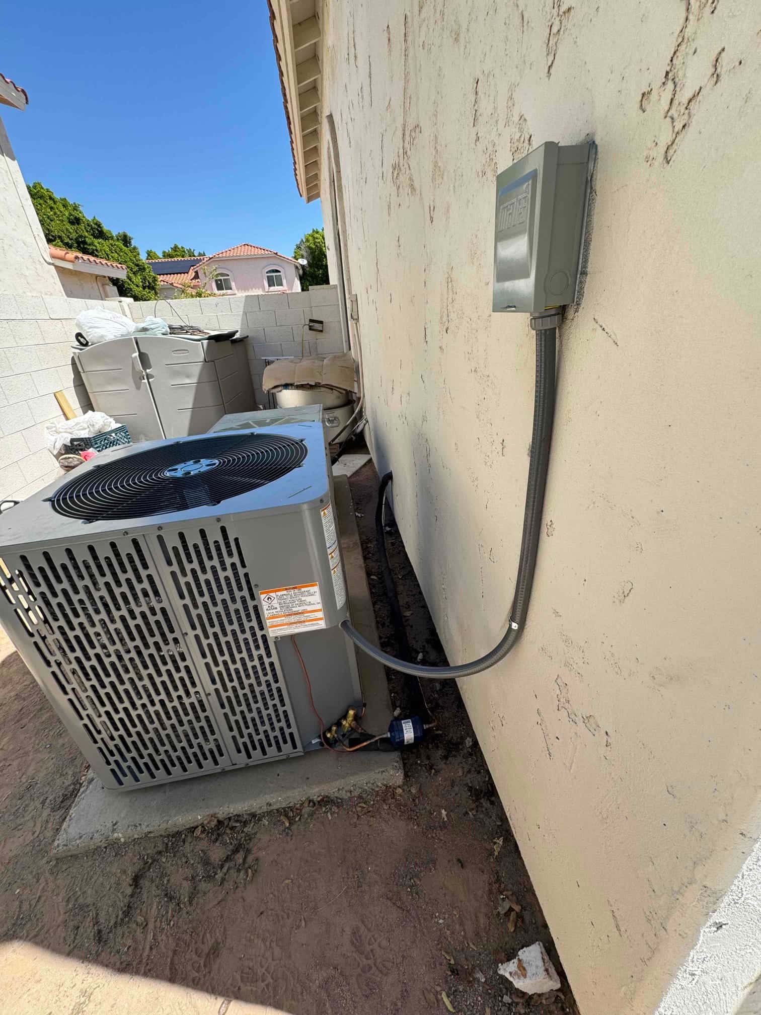 New outdoor condenser installed on a level pad with weatherproof electrical disconnect and insulated line set routed along the wall.