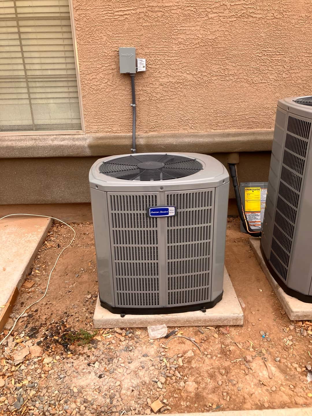 New outdoor condenser set on a level pad with armored disconnect whip and sealed wall penetration at the installation site.