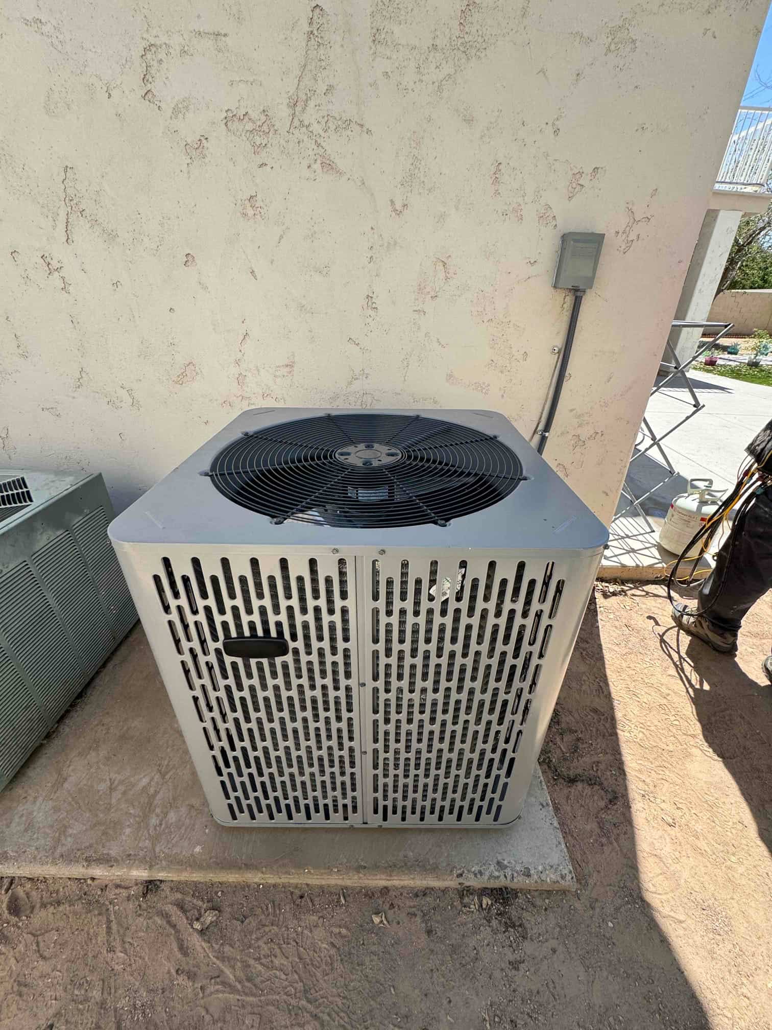 New outdoor condenser set on a level pad with electrical disconnect mounted on the wall and line set routed.