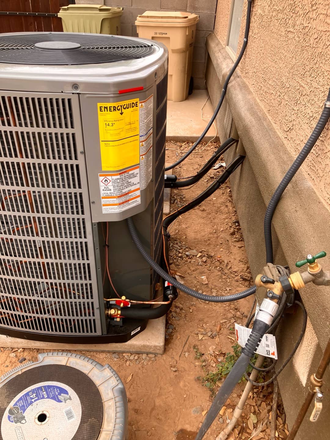 New outdoor condenser set on a level pad with insulated refrigerant lines and electrical whip routed along the exterior wall.