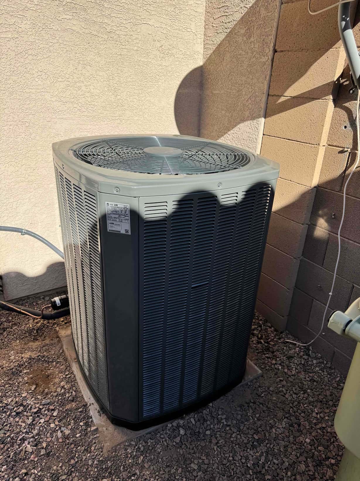 New outdoor heat pump condenser set on a level pad with connected refrigerant lines and electrical whip.