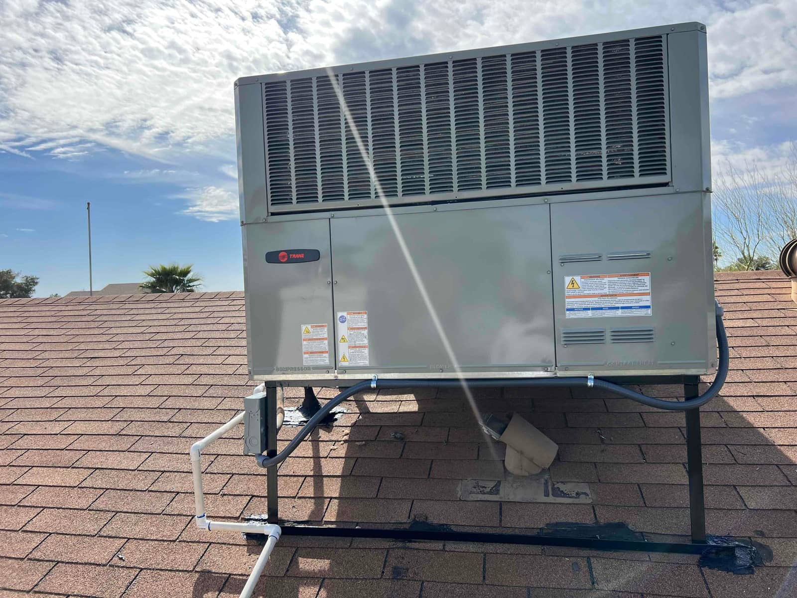 New rooftop package heat pump set on a steel stand with insulated refrigerant lines and PVC condensate drain routed across shingles.