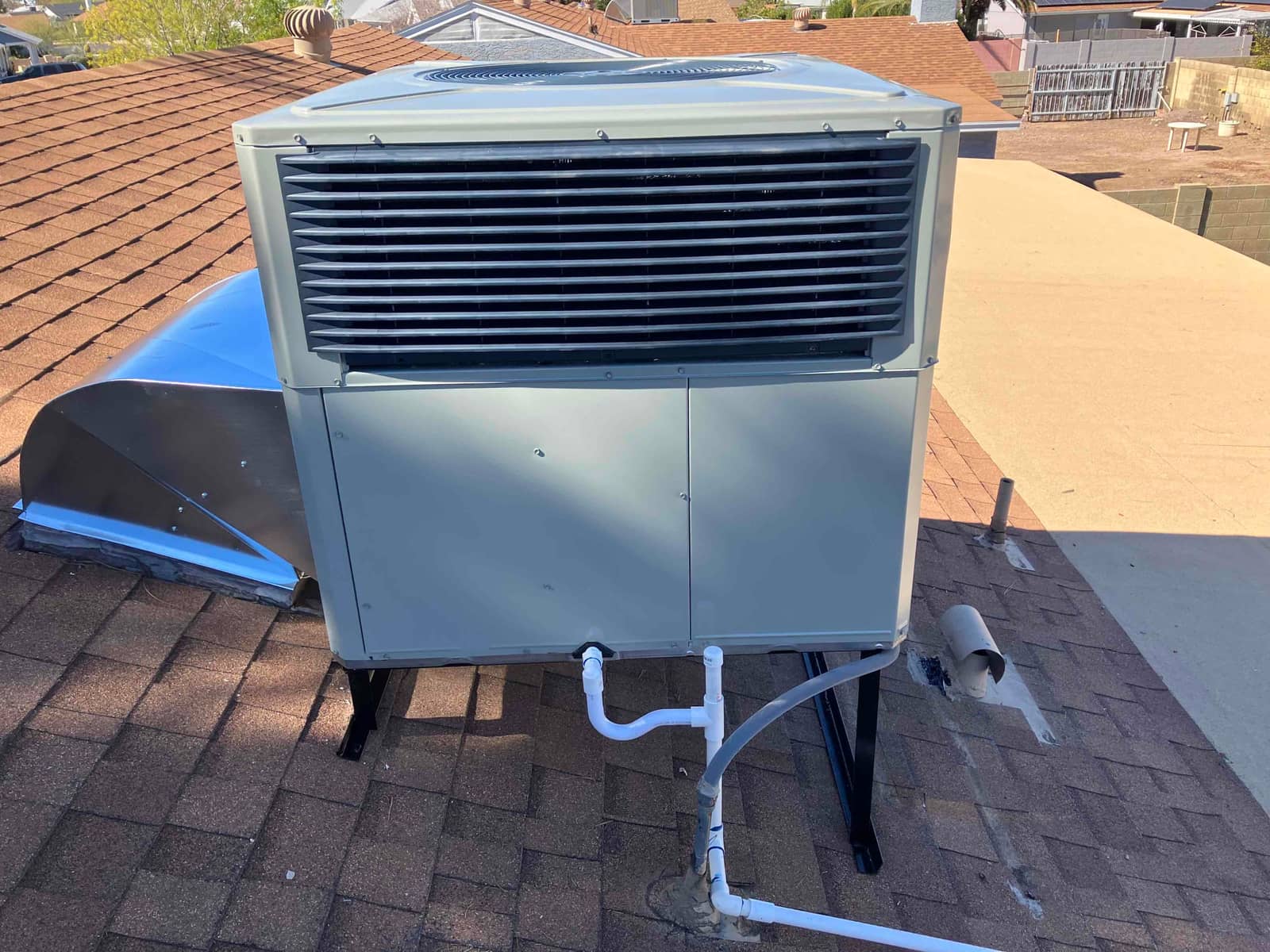New rooftop package unit installed on a stand with connected condensate drain and curb transition on a shingle roof.
