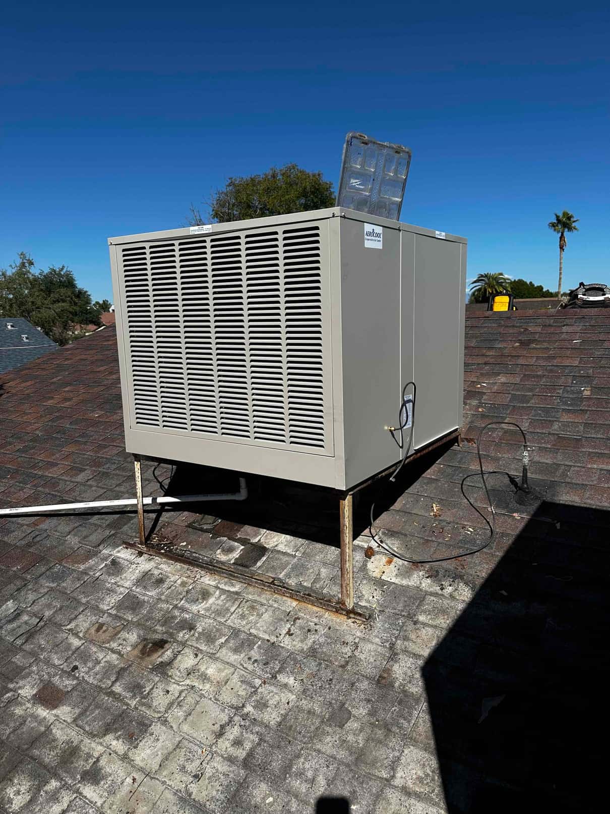 New rooftop package unit set on raised rails with connected condensate drain and electrical whip, photographed after installation.