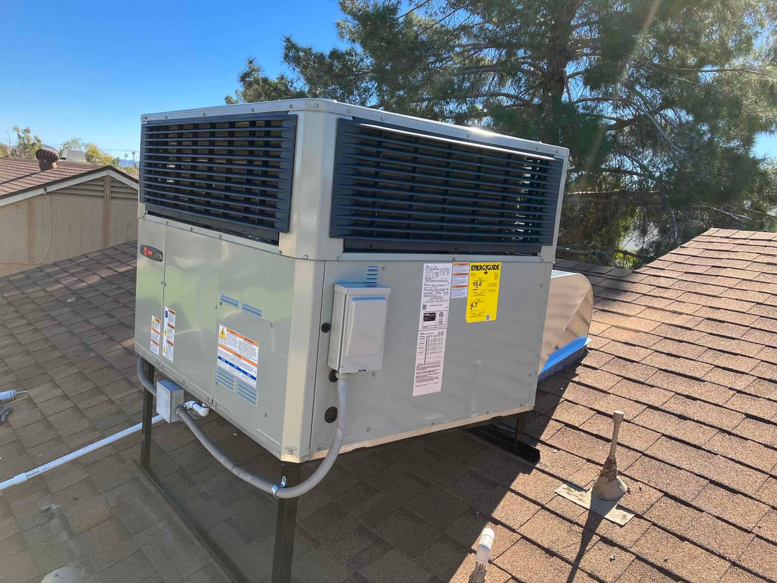 New rooftop packaged heat pump installed on a metal stand with electrical disconnect, flex conduits, and roof curb connection.