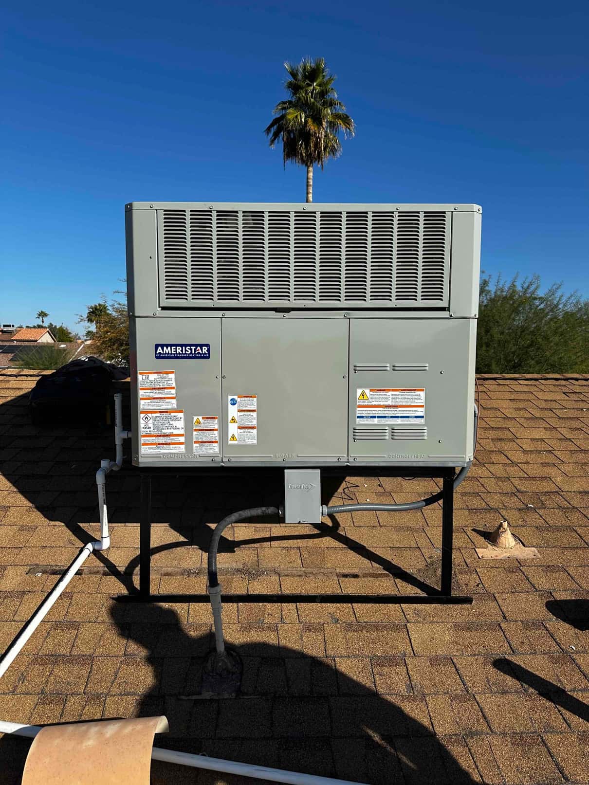 New rooftop packaged HVAC unit mounted on a metal stand with electrical disconnect and condensate drain piping routed along the roof.
