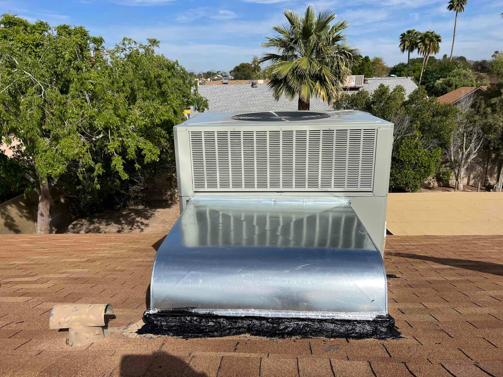 New rooftop packaged unit installed on curb with sealed supply/return duct transition and weatherproof flashing on the shingle roof.
