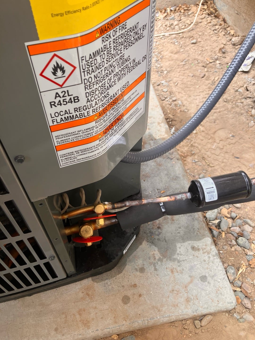 Outdoor condenser connections with service valves, insulated suction line, and liquid-line filter-drier mounted on a level pad.