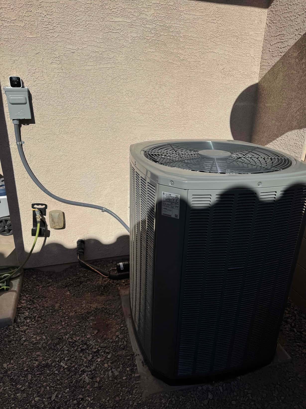Outdoor heat pump condenser installed on a level pad with whip to the disconnect and insulated refrigerant lines routed to the wall.