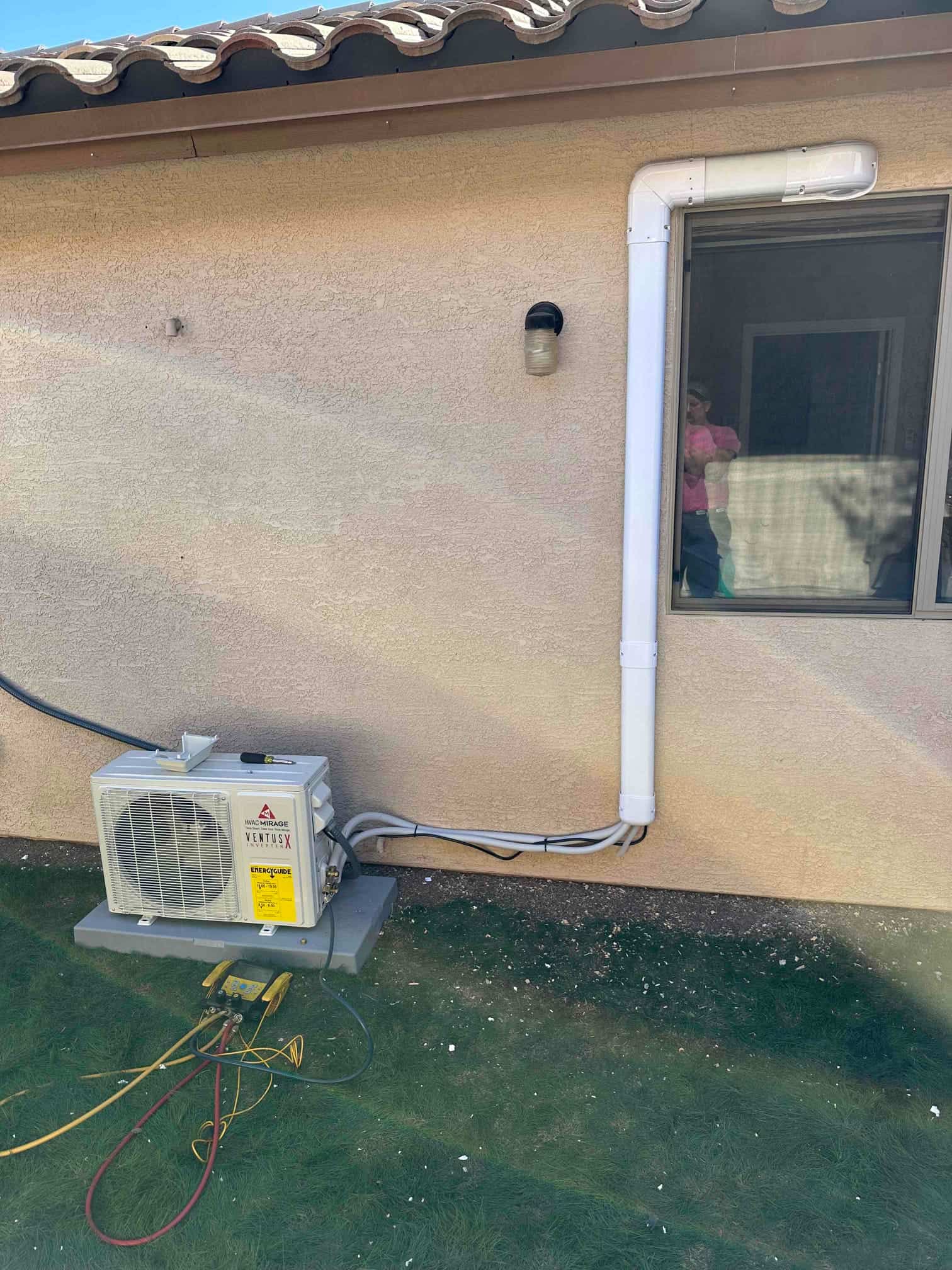 Outdoor heat pump condenser set on a level pad with line set in protective cover and refrigerant hoses attached.