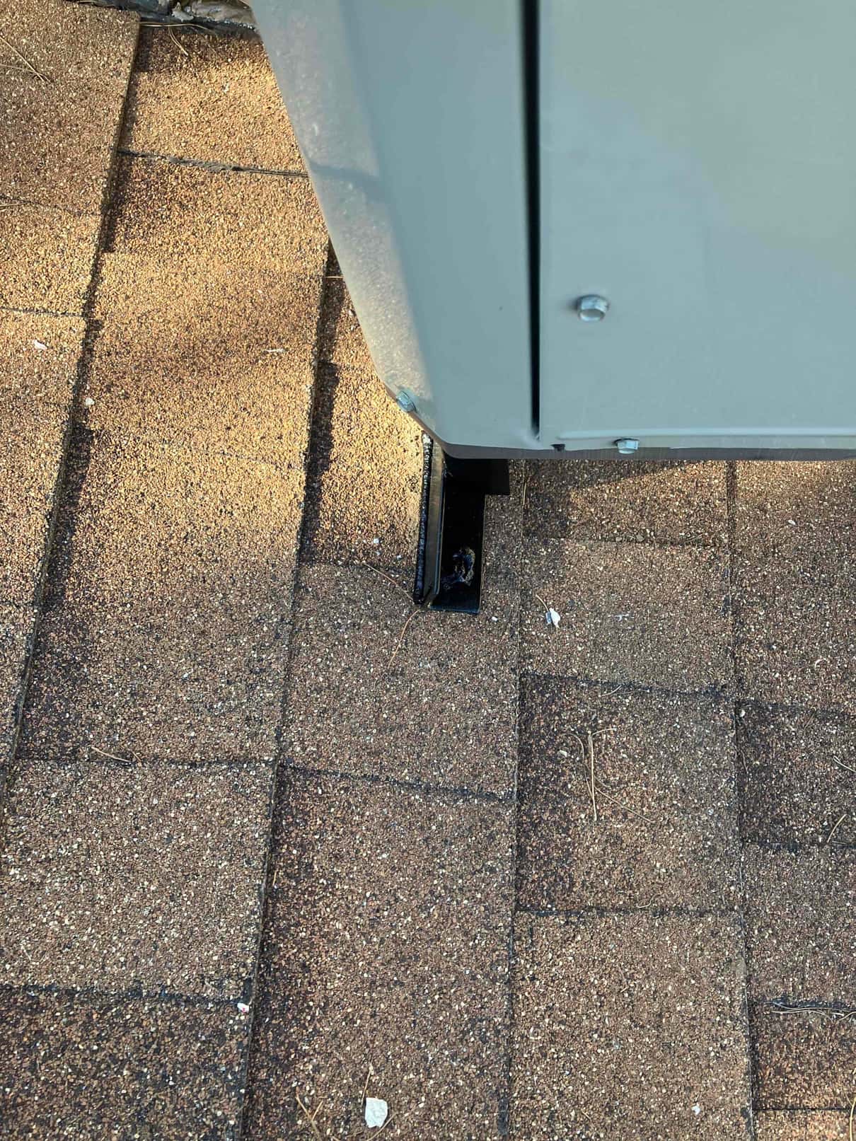 Outdoor unit corner mounted on a rooftop support foot, showing secure fasteners and placement on asphalt shingles.