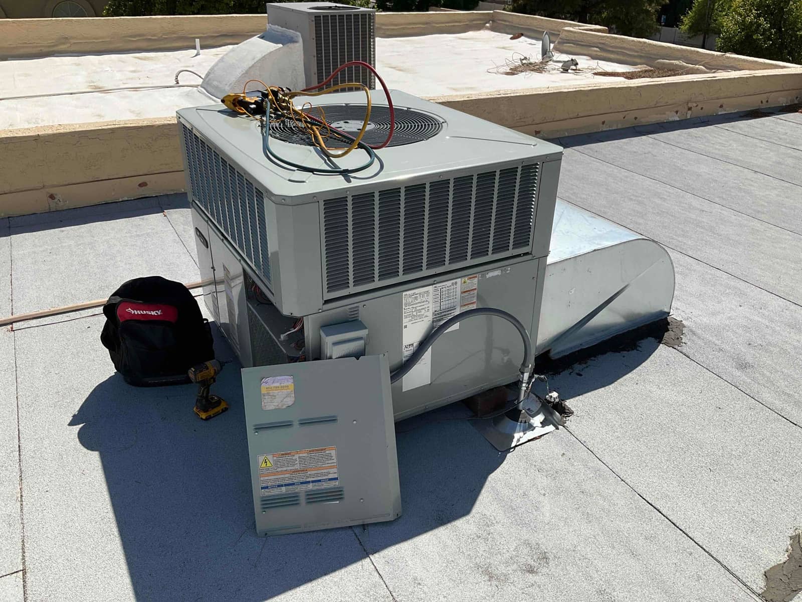 Rooftop HVAC package unit with service panel removed, manifold hoses and tools placed on top during inspection.