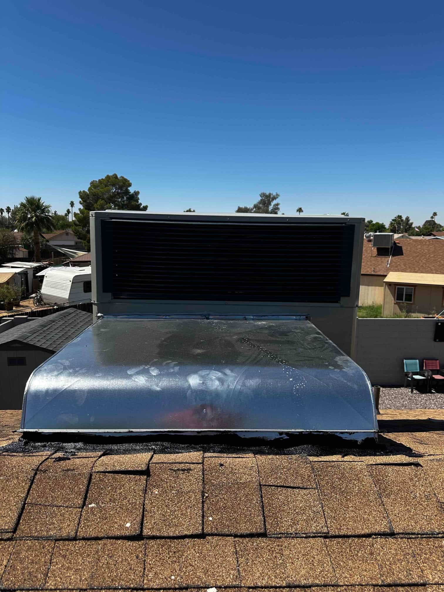 Rooftop package unit with new sheet metal curb and sealed roof penetration shown from the shingle ridge.
